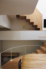 Staircase housing storage beneath it rises from basement area with piano, through mezzanine dining area and living area with thin white metal railing overlooking entryway and double-height cavity with white walls. to bedrooms on upper stories in the Hirano, Osaka, Japan home of Tsuyoshi and Maya Ohama designed by local firm FujiwaraMuro Architects with a split-level plan.