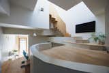 Entry of  the Hirano, Osaka, Japan home of Tsuyoshi and Maya Ohama designed by local firm FujiwaraMuro Architects leads through narrow hall with sink, up a short wood staircase to dining room with blue children's dining seat and dark-toned wood stool with taupe fabric seat embroidered with octagon pattern, and then up another flight of stairs to raised family living room, and up a final wood staircase through a double-height space to bedrooms above.