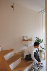 Man sits on wood step of short staircase beside wall-mounted sink and stool with green laminate top past entry into the Hirano, Osaka, Japan home of Tsuyoshi and Maya Ohama designed by local firm FujiwaraMuro Architects.