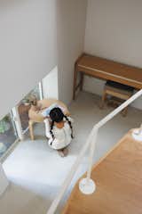 Child draws at low, triangular table with rounded edge beside floor-height window and piano in an office situated in a corner with concrete floors and white walls beneath a raised living room in the Hirano, Osaka, Japan home of Tsuyoshi and Maya Ohama designed by local firm FujiwaraMuro Architects.