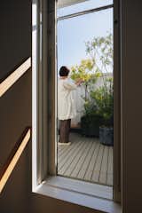 Woman tends short trees in white-tile floored terrace atop in the Hirano, Osaka, Japan home of Tsuyoshi and Maya Ohama designed by local firm FujiwaraMuro Architects.