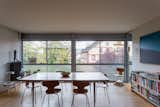 Dining and living room in an apartment in the prototypical urban residential apartment building the Immeuble Clarté in 1932, a now UNESCO World Heritage site in Geneva, Switzerland commissioned by Edmond Wanner and designed by Le Corbusier and his cousin Pierre Jeanneret, with large long table surrounded by wooden dining chairs, abstract figural sculptural set on tall grey radiator in the corner, a metal mushroom lamp and a bluish translucent case set atop low white tray tables, a blue and navy geometric painting, a combined media cabinet and bookshelf, and a row of floor-to-ceiling glass windows with the lower half set with translucent glass panes.