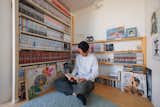 Man reads manga comic book in small, bright room with white walls, light hardwood floors, round grey rug, and shelves housing library of manga comic books, artwork, and figurines in the Hirano, Osaka, Japan home of Tsuyoshi and Maya Ohama designed by local firm FujiwaraMuro Architects.
