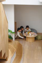 Children play videogame at low round table with faceted edges in family living room with light hardwood floors at bottom landing of staircase that rises through double-height space with white walls and large skylight in the Hirano, Osaka, Japan home of Tsuyoshi and Maya Ohama designed by local firm FujiwaraMuro Architects.