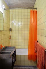 The bathroom has its original terrazzo floors, punched up with yellow tile, decor and fixtures in Day-Glo orange, and a custom steel sink.