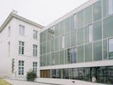 Exterior of a midcentury, neo-Breton post office building designed by architect Peirre-Jack Laloy and renovated into senior housing by Paris firm Chatillon Architectes in Brest, France with central modern volume clad in glass blocks and recessed away from the street flanked by two traditional three-story wings painted white.