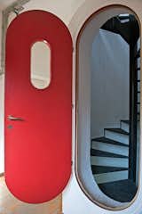The home’s primary accent color, also original to the design, is an orange-red that brightens window frames, doorways, and doors, like the rounded one leading to a concrete-encased spiral staircase.