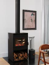 A black wood burning stove sits beside abstract figural drawing on pink paper with black frame in the dining room of a prefab home designed by architect Gabriele Mary Ann Schicketanz built from modular units by Method Homes in Carmel, California.