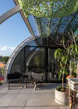 Atop the original, two-story concrete structure, the showstopping curved roof opens at the center and holds a studio at either end for the remote-working couple. “This was the greatest thing,” says Amalia. “Before, we always shared a studio, but Mauricio and Matías proposed that we each have our own space.” The garden, filled with species that Uzi collected from across Uruguay, climbs the mesh panels in front of the second floor.