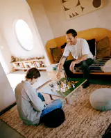 Artist Aaron Glasson and a friend relax in the 1950s Joshua Tree–area homestead cabin he and fellow artist Prescott McCarthy turned into a part-time home and artist residency. Aaron made the daybed, chess table, and artwork on the wall.