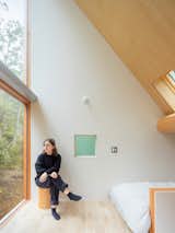 Office staffer Athénaïs Mieg de Boofzheim sits in the primary bedroom, where a horizontal support beam runs beneath the pitched ceiling—“It steadies the whole room,” says Rob—and large windows reinforce the home’s connection to nature.