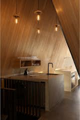 <span style="font-family: Theinhardt, -apple-system, BlinkMacSystemFont, &quot;Segoe UI&quot;, Roboto, Oxygen-Sans, Ubuntu, Cantarell, &quot;Helvetica Neue&quot;, sans-serif;">Robust enough to withstand the rugged site—and two big dogs—the concrete floors store radiant heat and age beautifully over time.</span>The kitchen is compact yet functional, anchored by hand-poured concrete waterfall countertops that flow into the floors. Beyond, a breakfast nook doubles as a workspace. Though the entry feels compressed, the public space gradually expands—growing wider and brighter as you move through it.  Photo 17 of 23 in This Clever Twist on an A-Frame Cabin? It Started in a Classroom from This Clever Twist On an A-Frame Cabin? It Started in a Classroom