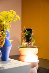 A blue vase by Hop & Jans Studio shares the stage with a vase by Andi Kovel / Esque Studio, a table by Peaches the Studio, and a lamp by Pigeon Toe Ceramics.