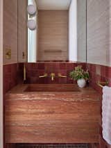 In the powder room, a red travertine motif continues from the floor up to the slab sink.