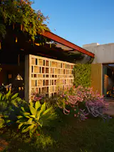 A geometric brise-soleil filters sunlight and casts shapes across a patio, which is enclosed on one side by a stone wall.