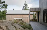 Glacier boulders and granite outcroppings are integrated into the design. Here, the home’s silvery exterior matches rock formations. Firewood stacks beneath an overhang framing the entry.