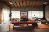 The sloped ceiling over the brick-walled living room is new. Below it, a walnut slat bench joins a vintage leather sofa, a Rush House seagrass rug, a Bertu Home Suelo side chair, and Bettina Chow Pottery vases. The Kelvin Floor Lamp is from Flos.