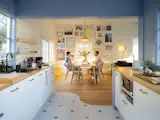 The couple updated the galley kitchen with new Ikea appliances and cabinetry and used a signature curved line to separate the wood floor from black-and-white Merola tile. They used paint from HGTV Home by Sherwin-Williams for the interior walls—Notable Hue in the kitchen and White Flour in the dining room. The Lisabo dining table and chairs, as well as the Varmblixt wall-mounted light, are from Ikea. The Roman window shades with valance are from Arlo Blinds, the yellow Tam-Tam Stool in the corner is by Henry Massonnet, and the pendant lamps are from Hampton Bay.