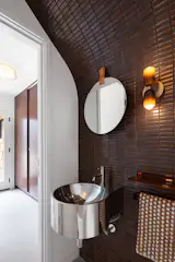 Burgundy Heath tile envelops one wall in the powder room, which is part of the entry. The industrial-style polished steel sink is from Lacava and the sconce is by In Common With.