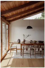 The dining area lies between the open kitchen and the sliding doors to the backyard, which are often left open. The table was a hand-me-down from a friend. She was selling her matching Hans Wegner chairs to go with it; they bought dupes instead. When they had trouble finding a light fixture for the space, Joe made one; it has opened up a new avenue for his art. All of the pottery is by Joe, except for the footed vase, which is by Amikar Palacios Salas.