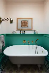In the upstairs guest bathroom, a Heritage Tiles pattern designed by Anderson pairs with wainscoting painted in Arsenic and a tub finished in Pink Drab, both from Farrow & Ball.