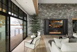 The fireplace wall introduces one of the home’s strongest vertical material moments, balancing the openness created by the surrounding glass.