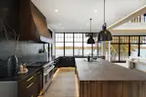 Dark cabinetry, walnut detailing, and oversized windows ground the kitchen within the home’s broader palette of organic textures and lake-facing light.