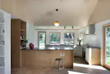 Lisa went with a Basis kitchen from Reform since it was more cost-effective than a custom one. To create the feeling of entering the kitchen within an open plan living area, Space4Architecture placed the cabinets in an “L” shape. “You are walking into the kitchen rather than passing through the kitchen,” Vici says. The LED Dipping pendant light is from Marset and the red ceramic vase is by Melissa Dadourian.  Photo 5 of 13 in Budget Breakdown: She Turned a Long Island Cottage Into a Creative Retreat for $418K