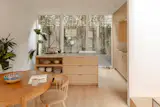 The dining area sits beside an internal picture window overlooking the double-height atrium with Muuto Rime pendants. A living green wall brings greenery into the space.