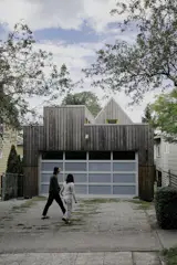 Exterior, House Building Type, ADU Building Type, Metal Roof Material, Wood Siding Material, Flat RoofLine, and Gable RoofLine Current tenants Evan Fleming and Lenore Wan walk past a custom garage door from Precision Door Service. It has one row of clear glass and three rows of frosted. "The idea was to provide enough light to allow the garage to be flexible in its use, especially as a workshop or workspace," says Kostic.&nbsp;The Toldbod 155 outdoor wall lamp is by Louis Poulsen.