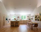 The kitchen countertops are lined up under a space that juts out from the main rectangular volume of the house. Between the asymmetrical windows is a photograph of a man eating strawberries by artist <a href="https://www.artsy.net/artwork/alex-da-corte-activity-number-9">Alex Da Corte</a>.