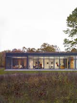 The glass-enclosed side of the house looks into a screened porch on the left, followed by a combined open space that brings together the living space, dining area, and the kitchen.
