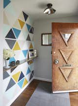 Carly and Brad rearranged the former entry closet area to form a small vestibule that would block the direct view to the kitchen upon arrival. Instead of covering it with wallpaper, they created a custom stencil and painted it themselves on Cristmas Eve. They used the colors that are used throughout the house, while the triangles take cues from the triangles that exist on the original door.