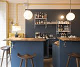 A set of wall-mounted String shelves, an iconic 1949 design by Nisse Strinning, provides storage for the casual bar, which features stools from By Lassen and wooden countertops.  Photo 4 of 6 in A Parisian Seafood Restaurant, Swimming in Shades of Blue