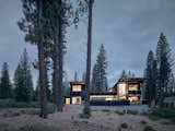 The structure is divided into two solid vertical volumes connected by glazed living areas. The cedar cladding and steel panels reflect the hues of the surrounding forest.