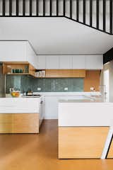 This Australian home received a mid-century modern update from Nest Architects. In the Kitchen white wardrobe cabinets with a light wood bottom, help make the space feel more open.