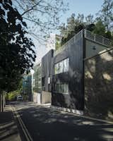Valhalla is a minimal residence located in London, England, designed by Denizen Works. Denizen Works were commissioned to transform the front elevation of a tired house in Highgate to complete a triptych of varied architectural approaches. Adjacent to our clients’ property there are two widely acclaimed pieces of contemporary residential design. Our clients had grown weary of comparison to their neighbors and asked Denizen Works to give new life to their street elevation converting it from a tired piece of mid-twentieth century modernism to a contextual and poetic piece of architecture. Viewed from up or down the hill, the new elevation appears closed, but on moving past the house, a ghost of the original house is visible. The project references the nearby Highgate cemetery and plays on the reflective material qualities of the immediate neighbor. The charred larch creates a contrast between the two properties, one reflecting the living trees opposite and ours clad in black, traumatized wood.