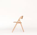 Narin Chair is a minimal chair created by England-based designer David Irwin. The elegant design features a smooth sweeping transition from the turned oak legs into the formed backrest, which also doubles as the mount for the pivot from where the back leg rotates. The seat and back are formed from layered birch ply with an oak veneer with an oiled finish and stainless steel fixings. The fixings contained on the underside of the chair slide along the grooves within the back legs to present a graceful silhouette with clean flowing lines, which looks as good folded away for storage as it does when open and in use.