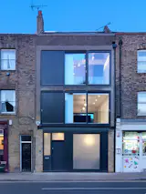 Fissure House is a minimal home located in London, United Kingdom, designed by Threefold Architects. Space was optimized by creating a single linear staircase occupying a triple height void or ‘fissure’ along the edge of the building. Internally, variety and excitement was achieved between floors by cutting back each floor plate to create dramatic views and glimpses of different living spaces. The character and materiality of existing brickwork was celebrated and complimented with new bespoke joinery and metalwork, embracing the strong craft tradition within the local area. New openings and external terraces were introduced at the rear transforming a once crowded and claustrophobic site into a spacious, light and multi-layered home.