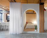 This small, L-shaped apartment by Studio AC has a bed box with an arched doorway with white walls and plywood finishings. 
