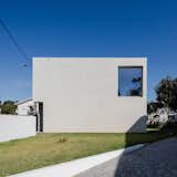 Mami House is a minimalist architecture project located in Porto, Portugal, designed by NoArq. The rectilinear concrete home was constructed on a very limited budget. As a result, extra effort was taken to make sure everything was kept as simple as possible. The staircase is situated towards the center of the home, and serves as a partition between the adjacent programs. Large glazings provide abundant natural light to the interior, and are framed in wood.