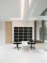 Notary Office is a minimalist space located in Ghent, Belgium, designed by Abscis Architecten. This new office building along the Kortrijksesteenweg in the green Sint-Denijs-Westrem includes a notary’s office with a studio above it. The building is a solid brick volume characterized by volumetric incisions and strategically placed windows. The glass ‘lantern’ at the top of the stairwell forms a minimalist light beacon along the busy road. The front façade opens up on the ground floor through the foyer towards the street, and welcomes visitors via a forecourt. This provides a great visibility and transparency. At the rear facade both the deed halls and the offices enjoy a beautiful view on the landscaped garden with old trees. The client’s request to have two waiting rooms adjacent to the deed halls resulted in an open plan. The patio works as a structural element to create privacy without taking away from the transparency of the plan.