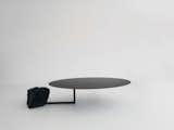 110kgs is a minimalist table created by Barcelona-based designer Max Enrich. 110 kgs is the weight of the black granite rock, used as a counterweight to hold a solid iron ellipse-shaped top. They meet in a cold joint, just by positioning the heavy rock on top of the leg of the table. The axis of the top is reinforced on the inside to keep is as thin as possible and carefully welded to the top to avoid deformations. The rock, obtained from remains of large pieces, reminds of a rock pulled out of a river, with soft edges and faces combining with other aggressive edges, shaped by water. Some irregular sides were left to recall to its origins, a large stone – to recall it was someday part of a bigger total.