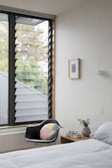 Bedroom, Bed, Night Stands, Wall Lighting, and Chair A Breezway Louve window brings air into a bedroom.  Photo 9 of 10 in A Family Home in Australia Features a Playful Version of the Classic Pitched Roof