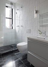 A Duravit vanity and Grohe faucet in the bathroom are paired with Catia Black marble tile on the floors, and floor-to-ceiling ceramic subway tile on the walls.