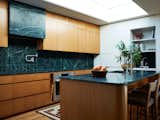 The kitchen features Vermont verde granite that has a bespoke pattern etched into it. Walnut cabinetry is contrasted with white paneling on either side.
