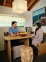 Rami Jrade and Hannah Go relax in the dining nook Hannah created in a corner of the open-plan living-dining room-kitchen. She found the bench and table online and the Akari pendant light from the Noguchi Museum website, and she made the cafe curtains with remnants from Ikea draperies. The stool was handcrafted by architect Hunter Knight, who designed and built the ADU. The painting is vintage.