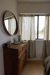 In the primary bedroom, an Ikea mirror found on a curb is set above a midcentury oak dresser the couple found on Facebook Marketplace. the gingham curtains are from West Elm.
