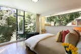 A corner bedroom's floor-to-ceiling windows allow sunlight to stream in, while the mature trees help maintain privacy.
