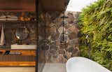 Bath Room, Freestanding Tub, Track Lighting, Vessel Sink, Concrete Floor, Wood Counter, and Stone Slab Wall Partially outdoors, the unconventional bathroom is a lush sanctuary.  Photo 11 of 14 in An Incredible Brazilian Home That Celebrates Art, Travel, and Nature
